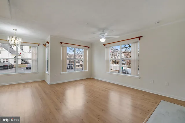 an empty room with wooden floor ceiling fan and windows
