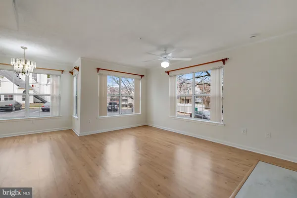 an empty room with wooden floor ceiling fan and windows
