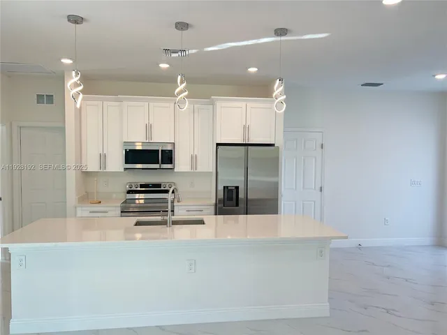 a kitchen with stainless steel appliances a refrigerator a stove a sink and white cabinets