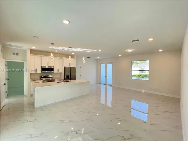 a large white kitchen with kitchen island a sink a stove a refrigerator and a dining table