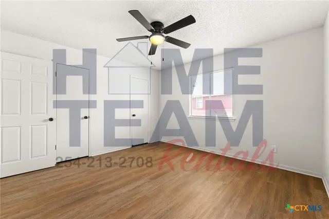 a view of an empty room with wooden floor and a ceiling fan