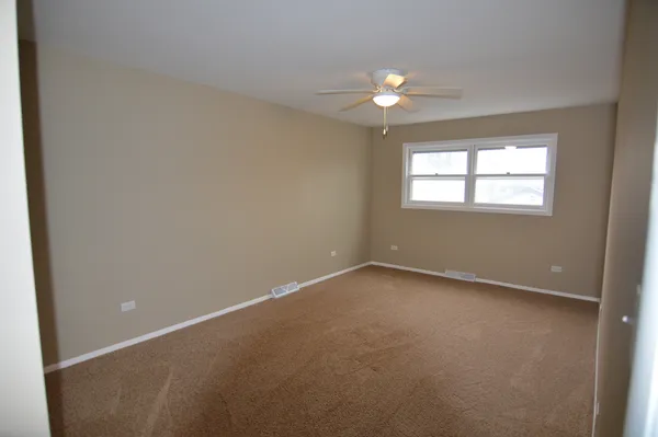 an empty room with a chandelier fan and windows