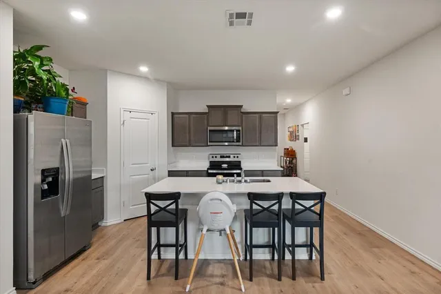 a kitchen with stainless steel appliances a dining table chairs refrigerator and microwave