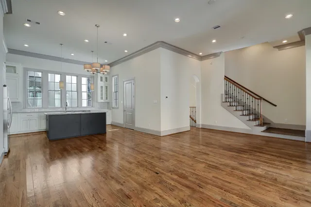 a view of an empty room with wooden floor and a kitchen
