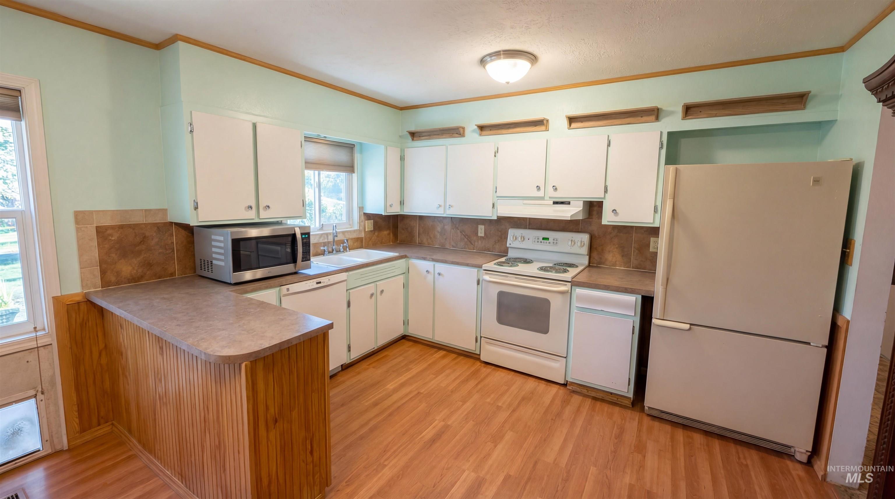 19076 Pleasant Avenue Caldwell, ID 83607 - Photo 7 of 37 Kitchen with white appliances, a peninsula, ornamental molding, light wood finished floors, and decorative backsplash