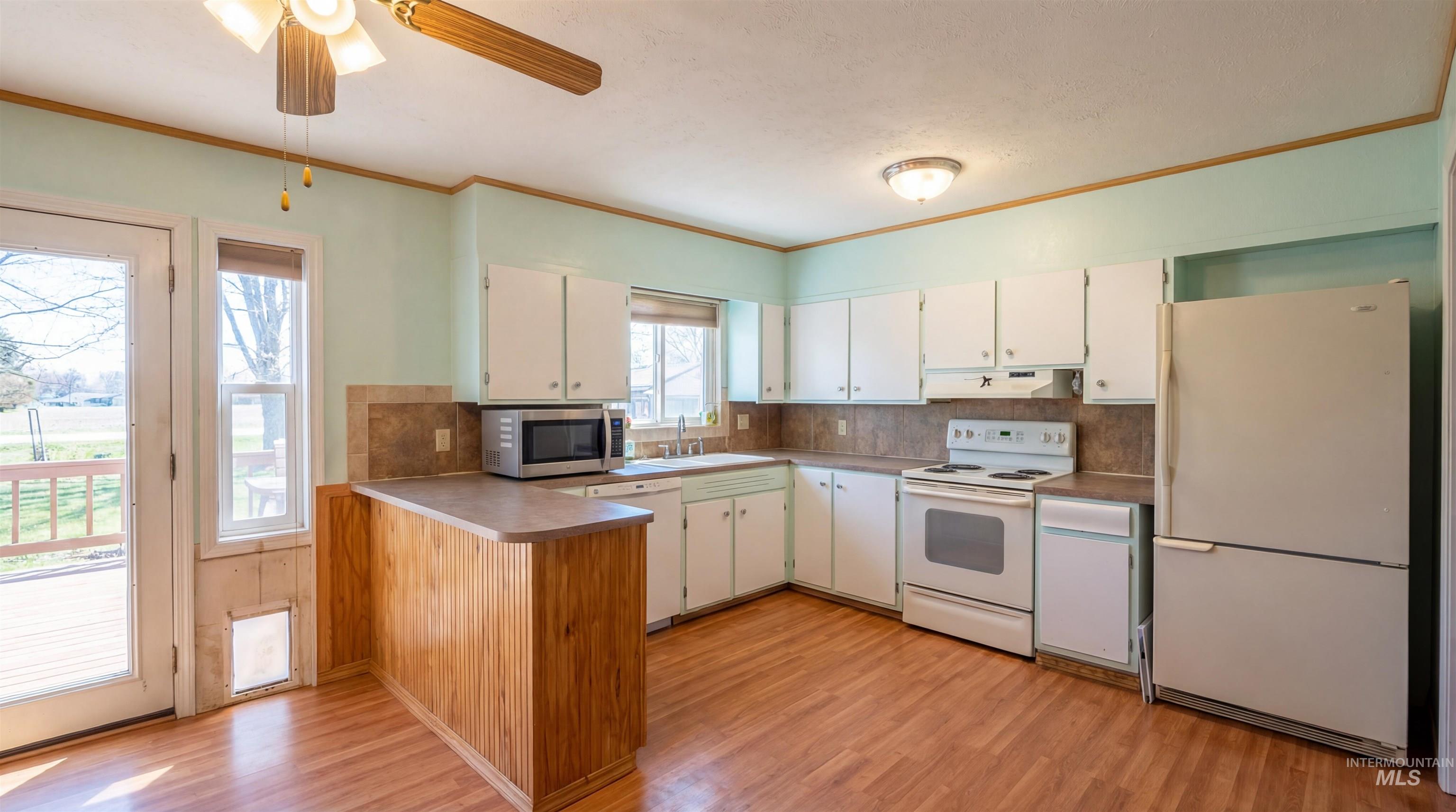 19076 Pleasant Avenue Caldwell, ID 83607 - Photo 9 of 37 Kitchen with a peninsula, white appliances, ornamental molding, light wood finished floors, and backsplash