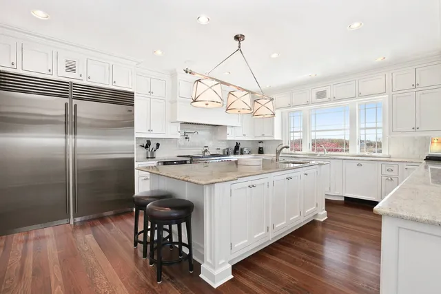 a kitchen with stainless steel appliances granite countertop a refrigerator a sink dishwasher a stove and white cabinets with wooden floor