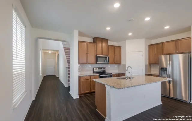 a kitchen with kitchen island granite countertop a sink stove refrigerator and wooden floor
