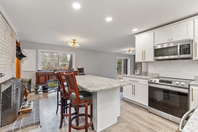 a kitchen with stainless steel appliances kitchen island granite countertop a stove top oven a sink a dining table and chairs with wooden floor