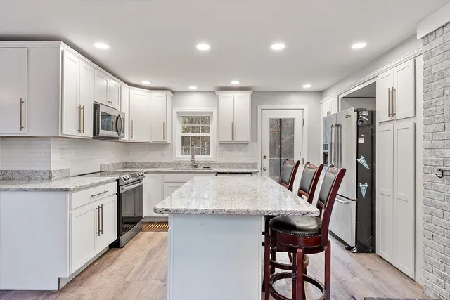 a kitchen with stainless steel appliances granite countertop a stove top oven a sink dishwasher a dining table and chairs with wooden floor