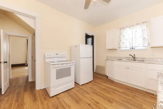 a kitchen with a sink a refrigerator a stove and white cabinets with wooden floor