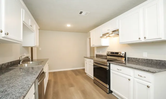 a kitchen with granite countertop a sink stainless steel appliances and white cabinets