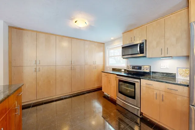 a kitchen with stainless steel appliances kitchen island granite countertop a refrigerator a stove a oven with white cabinets and wooden floor