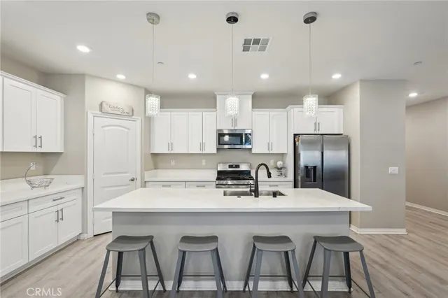 a kitchen with stainless steel appliances a sink a stove a refrigerator with white cabinets and wooden floor