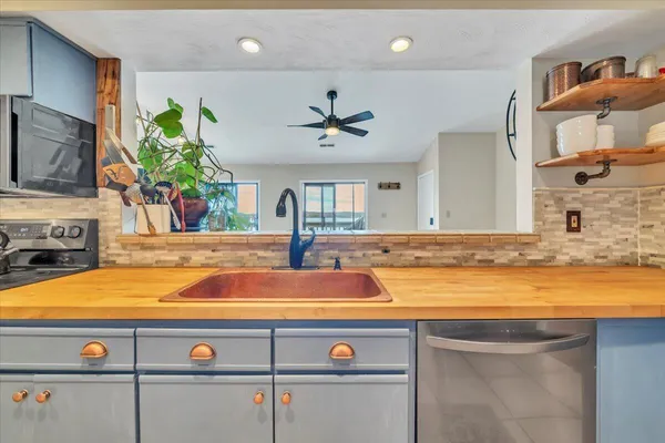 a view of a kitchen island with stainless steel appliances granite countertop a sink dishwasher and a stove with wooden floor