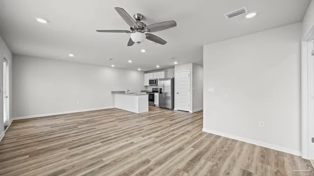 an empty room with wooden floor a ceiling fan and kitchen view