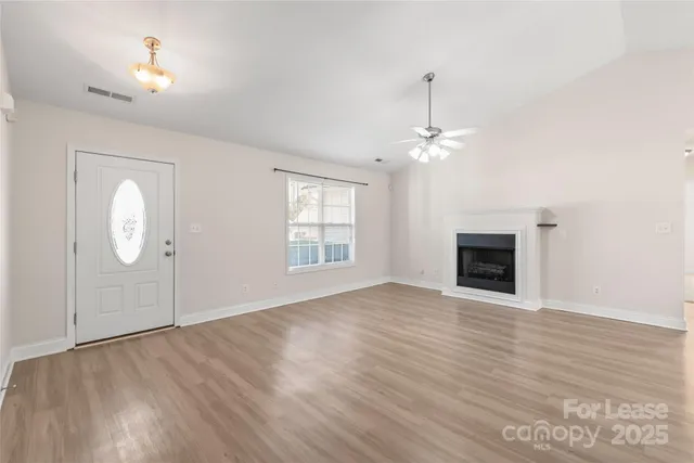an empty room with wooden floor fan and windows