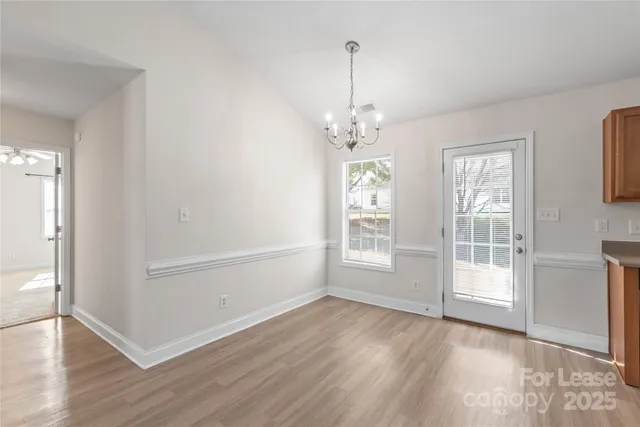 an empty room with wooden floor chandelier and windows