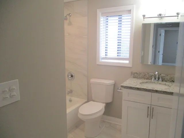 a bathroom with a granite countertop toilet a sink and a window
