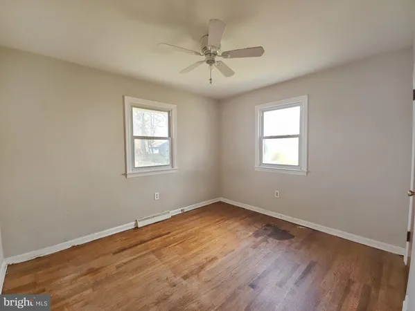 an empty room with wooden floor windows and fan