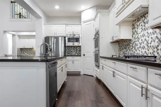 a kitchen with stainless steel appliances kitchen island granite countertop white cabinets a refrigerator and a sink