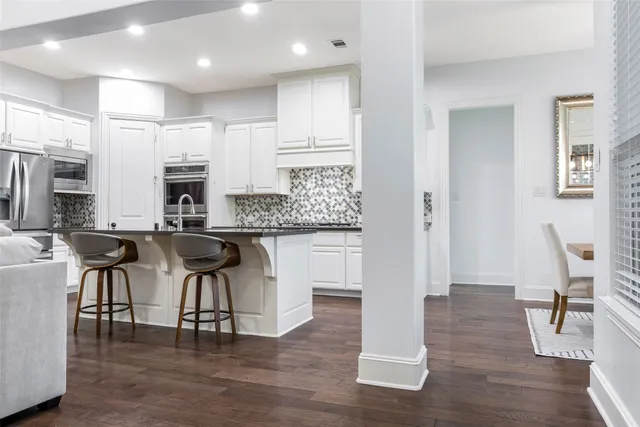 a kitchen with stainless steel appliances granite countertop a stove a sink a refrigerator and white cabinets with wooden floor