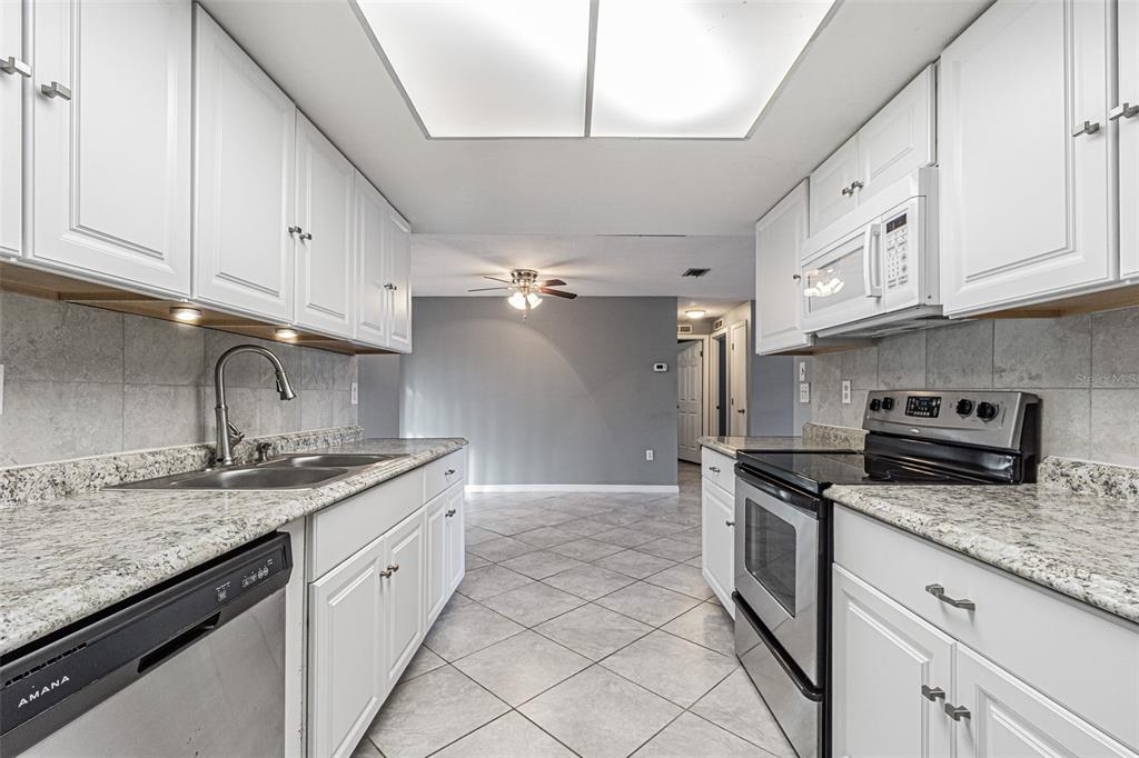 1529 Larkin Road Spring Hill, FL 34608 - Photo 13 of 37 a kitchen with granite countertop a sink stainless steel appliances and white cabinets