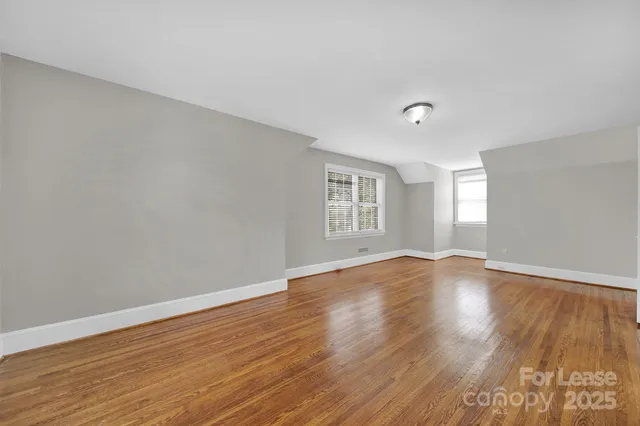 a view of an empty room with wooden floor and window