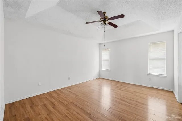 an empty room with wooden floor fan and windows