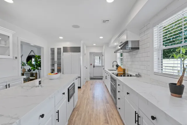 a large white kitchen with a large window a sink and stainless steel appliances