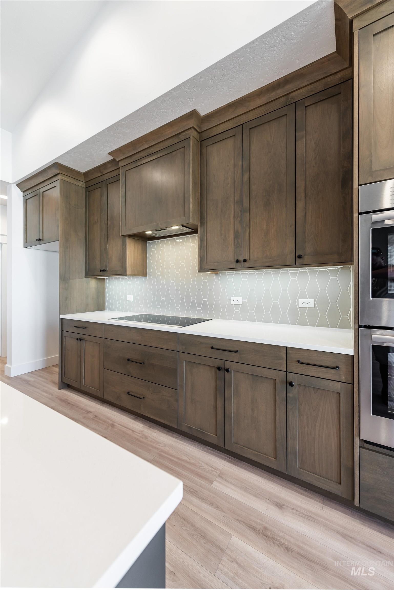 400 South Diesel Way Boise, ID 83716 - Photo 10 of 44 Kitchen featuring double oven, light wood-style flooring, dark wood finish cabinets, tasteful backsplash, and black electric stovetop