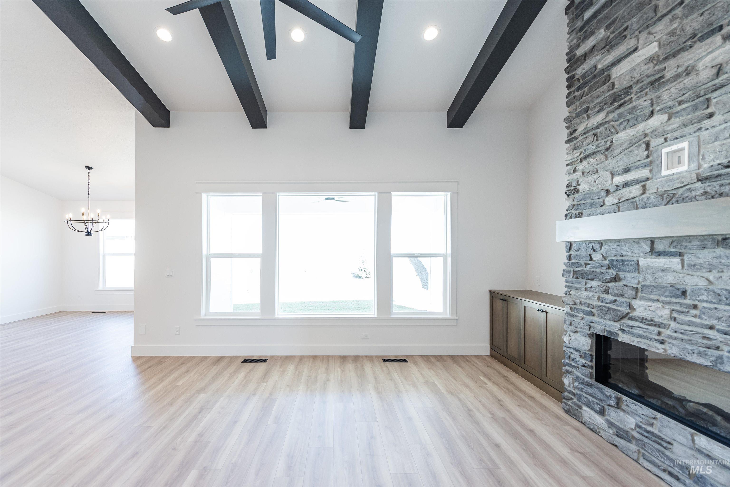 400 South Diesel Way Boise, ID 83716 - Photo 7 of 44 Unfurnished living room featuring a stone fireplace, light wood-type flooring, suspended lighting, plenty of natural light, and beam ceiling