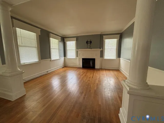 an empty room with wooden floor fireplace and windows