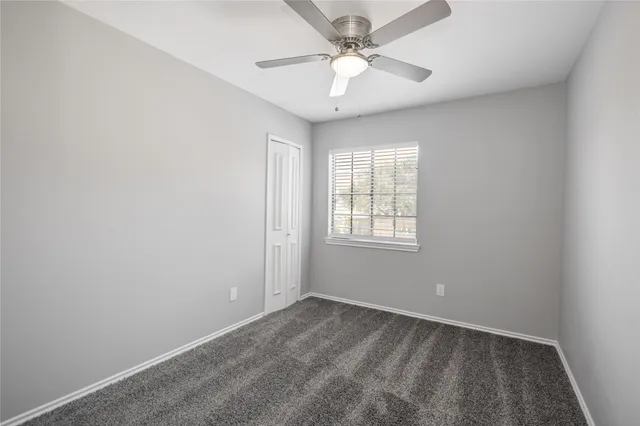 an empty room with chandelier fan and windows
