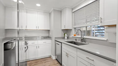 a kitchen with stainless steel appliances granite countertop a sink dishwasher a refrigerator and white cabinets with wooden floor