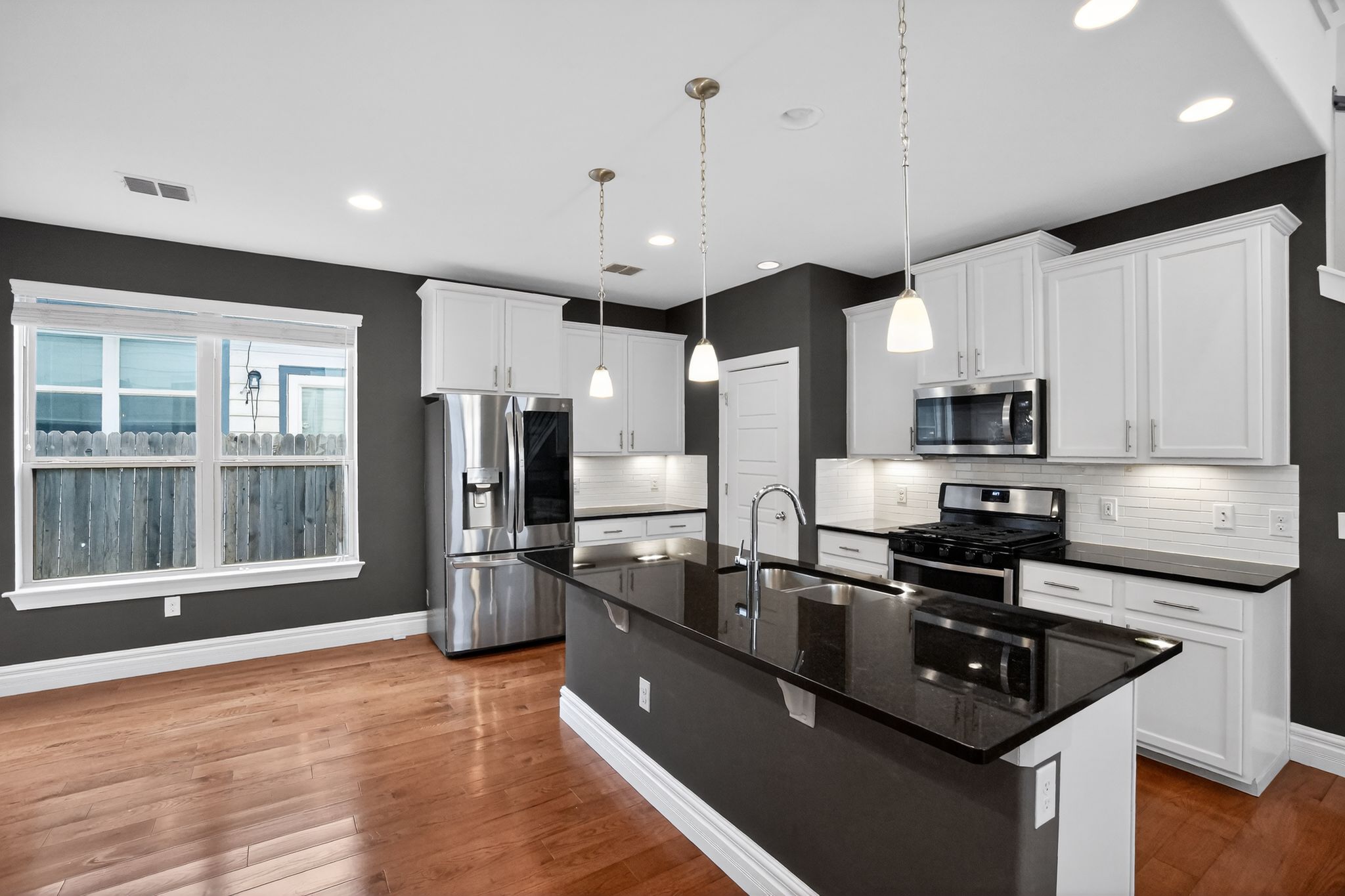 9717 Briny Shell Way Austin, TX 78748 - Photo 6 of 16 Kitchen with stainless steel appliances, dark stone countertops, an island with sink, white cabinetry, and dark wood-type flooring