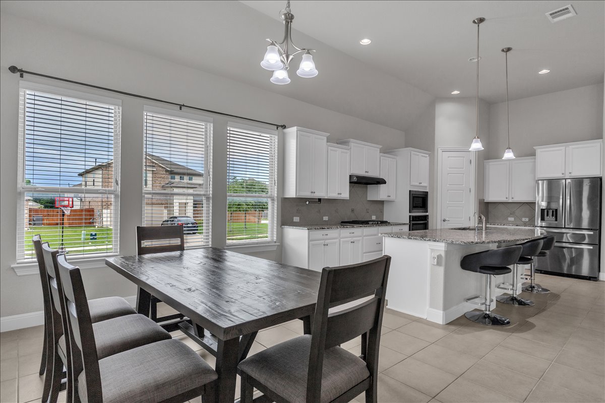 21301 Resource Road Pflugerville, TX 78660 - Photo 7 of 29 Open-concept kitchen and dining area featuring white cabinetry, stainless steel appliances, a large island with bar seating, and tile flooring