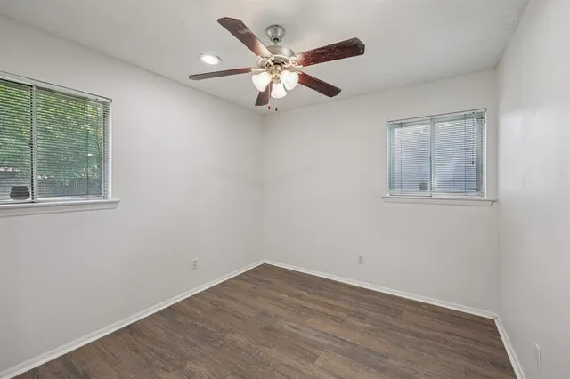 an empty room with wooden floor ceiling fan and windows