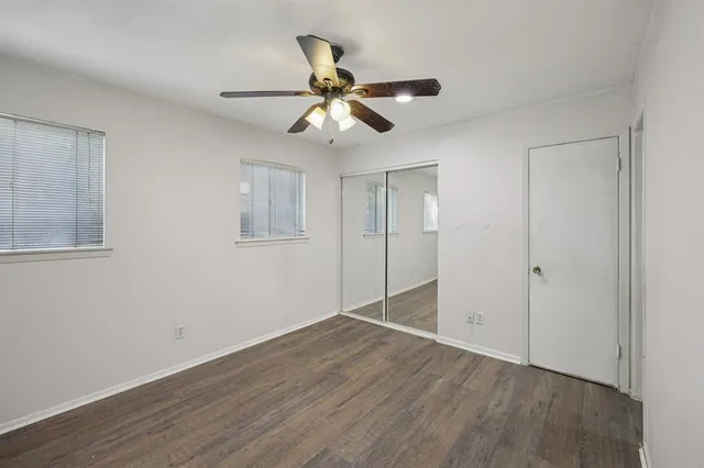 a view of an empty room with wooden floor and a ceiling fan