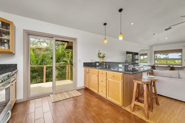 a open kitchen with granite countertop a stove top oven a sink a dining table and chairs with wooden floor