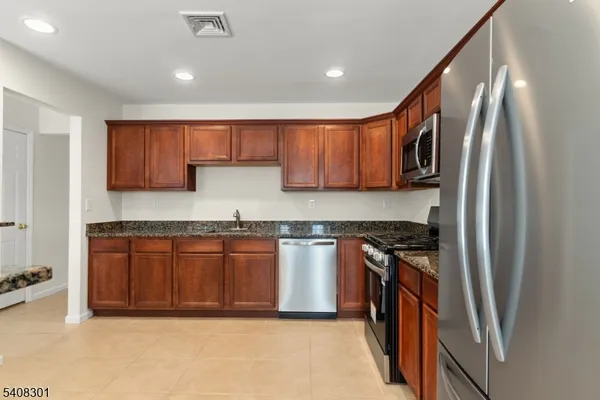 a kitchen with stainless steel appliances granite countertop a refrigerator a sink and wooden cabinets