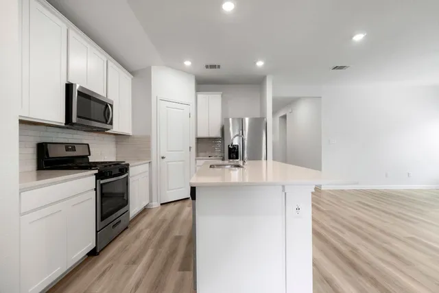 a kitchen with stainless steel appliances a stove top oven a sink a refrigerator white cabinets and wooden floor