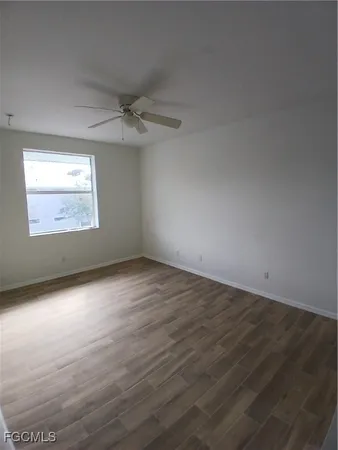an empty room with wooden floor ceiling fan and windows