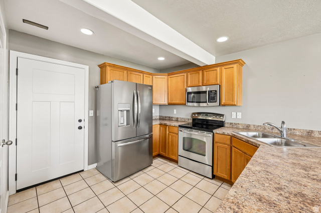 3215 West 450 North West Point, UT 84015 - Photo 11 of 40 Kitchen featuring stainless steel appliances, light wood cabinetry, a double basin sink, laminate countertops, and square tile flooring