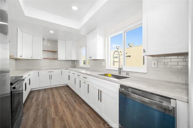 a kitchen with a sink dishwasher a stove and white cabinets with wooden floor