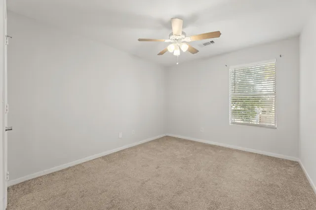an empty room with a chandelier fan and windows