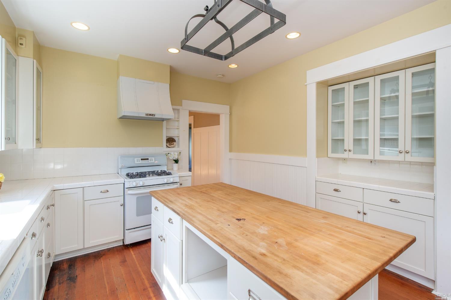 a kitchen with a stove a sink a refrigerator and white cabinets with wooden floor
