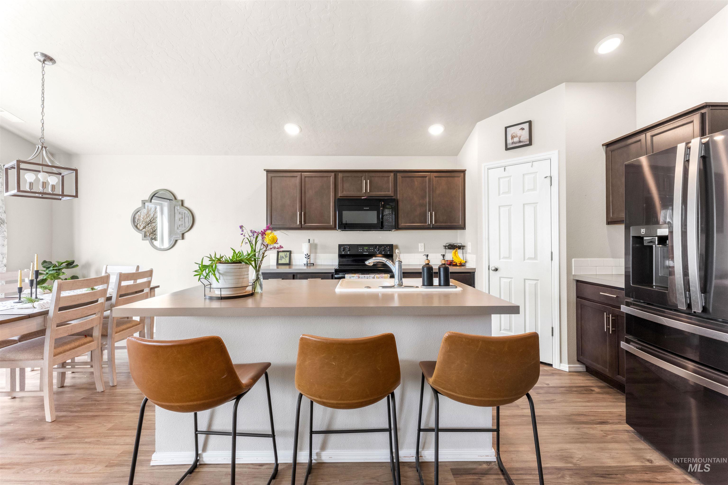 16378 Kelso Way Caldwell, ID 83607 - Photo 12 of 34 Kitchen featuring black appliances, dark wood finish cabinetry, light countertops, and a center island with sink