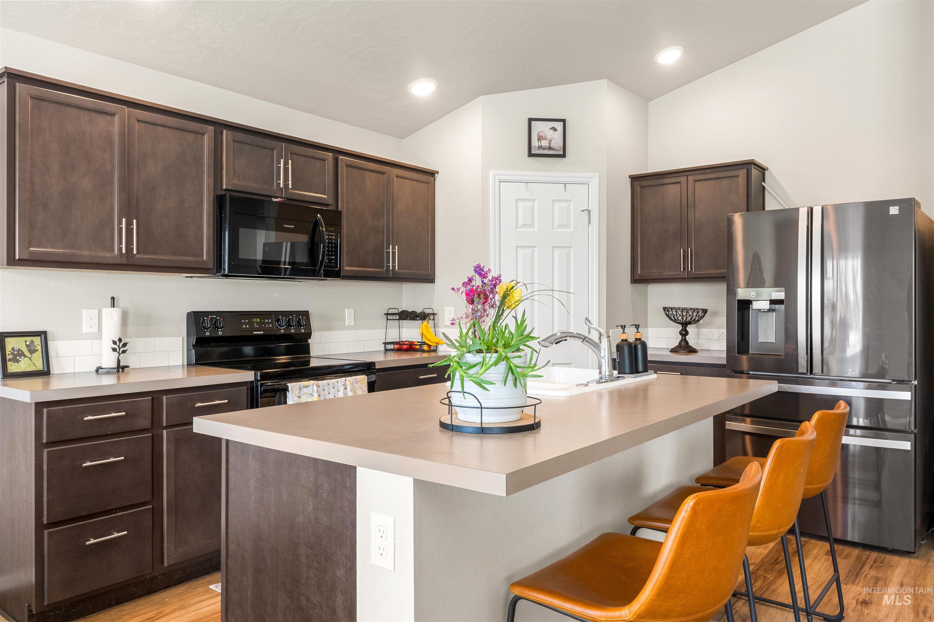 16378 Kelso Way Caldwell, ID 83607 - Photo 13 of 34 Kitchen featuring dark wood finish cabinets, black appliances, an island with sink, light countertops, and vaulted ceiling