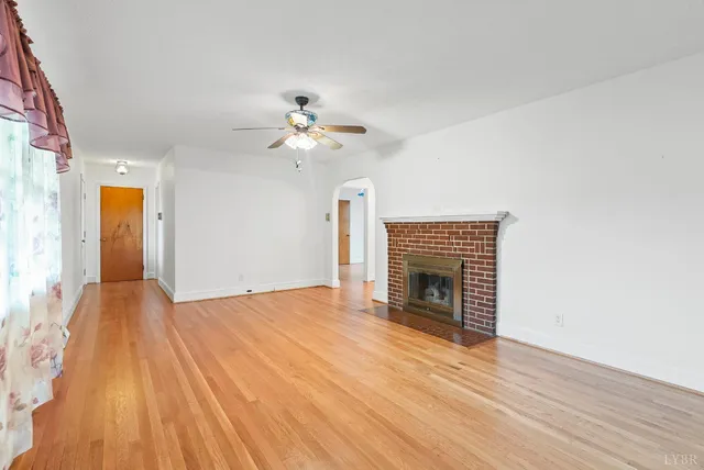 a view of an empty room with wooden floor fireplace and a window